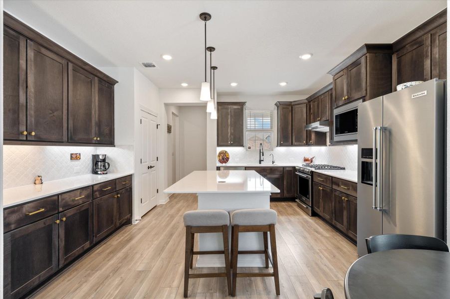 Kitchen featuring dark wood finish cabinets, high quality appliances, a kitchen breakfast bar, hanging light fixtures, and light wood-style flooring Kitchen featuring dark wood finish cabinets, high quality appliances, a kitchen breakfast bar, hanging light fixtures, and light wood-style flooring