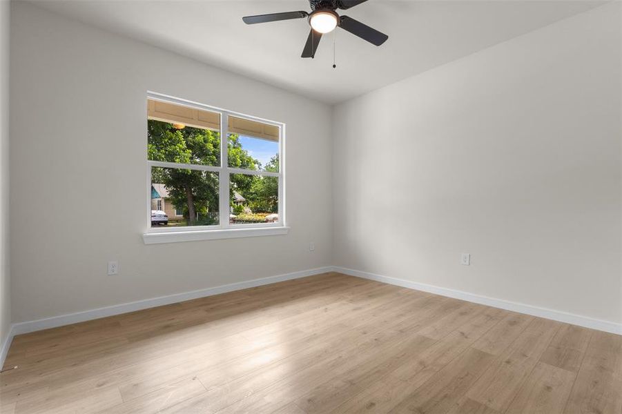 Spacious room featuring light wood-finish flooring, a contemporary ceiling fan, and a large window with white trim
