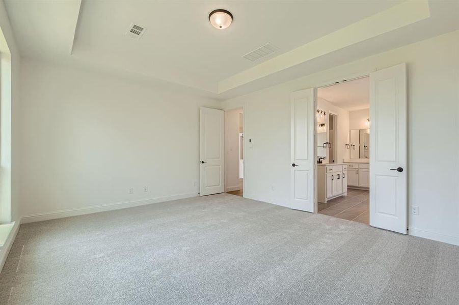 Unfurnished bedroom with light tile patterned flooring, ensuite bathroom, and a raised ceiling