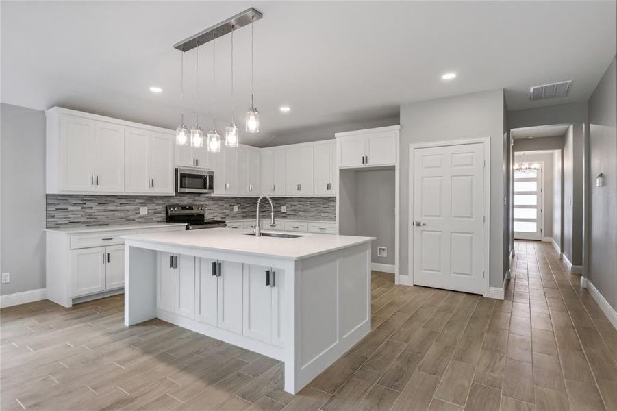 Kitchen featuring a center island with sink, stainless steel appliances, backsplash, and white cabinetry