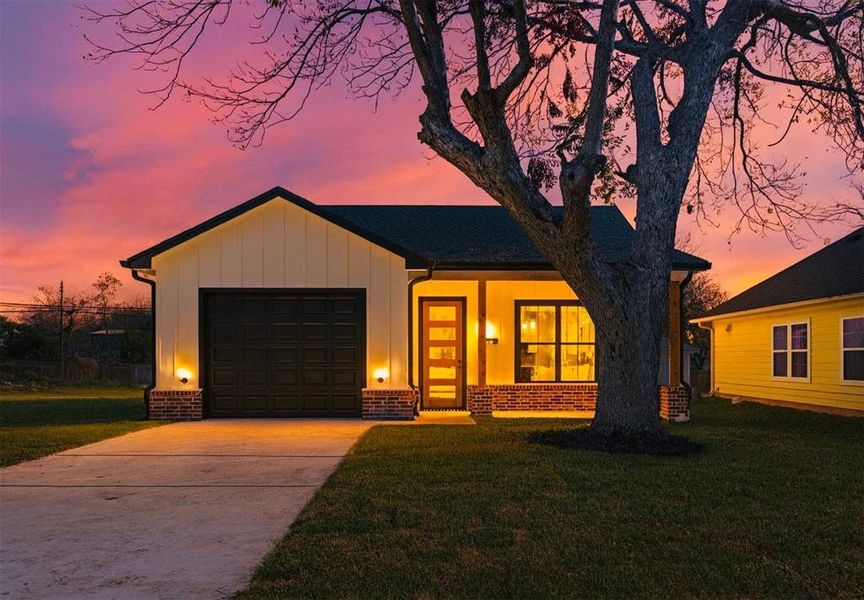View of front facade featuring board and batten siding, driveway, a lawn, and an attached garage