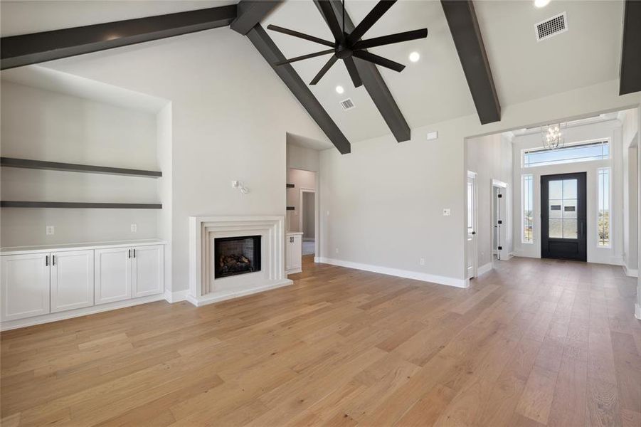 Unfurnished living room featuring high vaulted ceiling, light hardwood / wood-style flooring, beam ceiling, and ceiling fan with notable chandelier