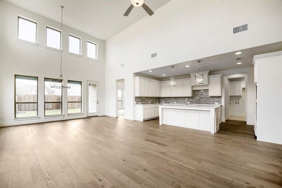 Spacious room featuring soaring ceilings, wood-finish flooring, and a kitchen with white cabinetry, a large island, and subway tile backsplash Spacious room featuring soaring ceilings, wood-finish flooring, and a kitchen with white cabinetry, a large island, and subway tile backsplash