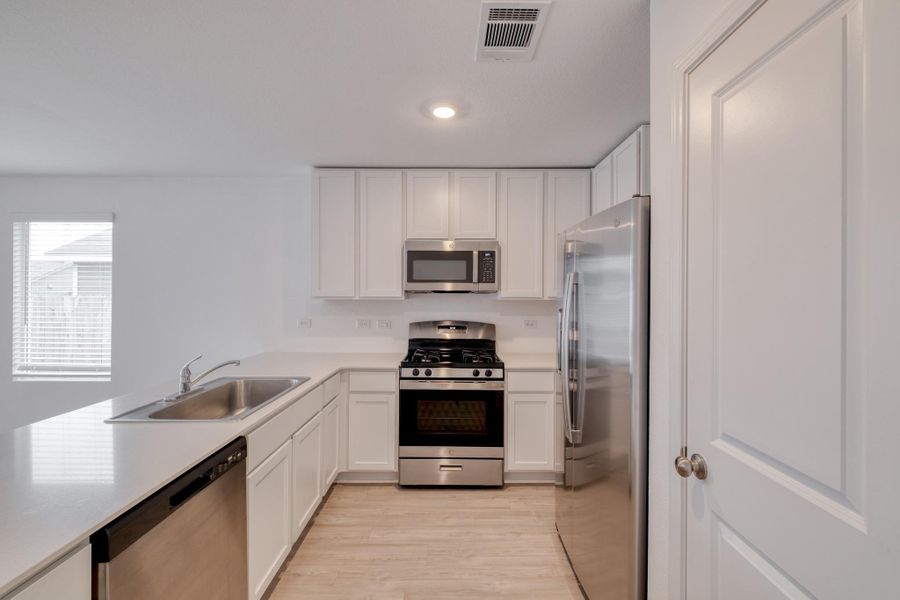 Kitchen featuring white cabinetry, light countertops, stainless steel appliances, a double basin sink, and wood-finish flooring