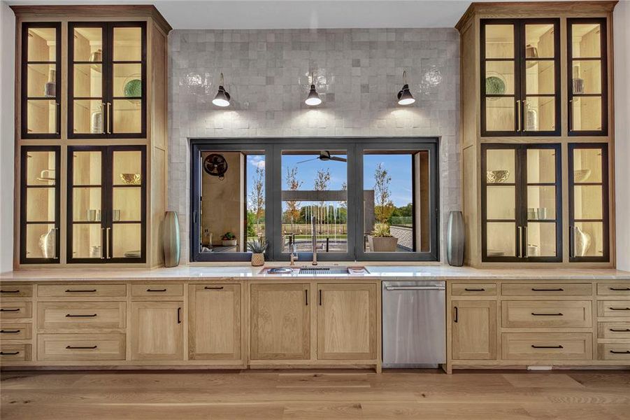 Bar area featuring glass insert cabinets, light brown cabinets, light wood-style floors, dishwasher, and light stone counters Bar area featuring glass insert cabinets, light brown cabinets, light wood-style floors, dishwasher, and light stone counters