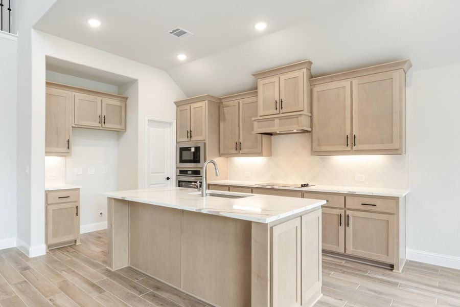 Kitchen with light tan cabinets, center island with sink, white countertops, and stainless steel wall ovens