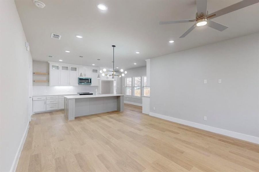 Kitchen with ceiling fan with notable chandelier, a kitchen island, light hardwood / wood-style floors, white cabinetry, and hanging light fixtures