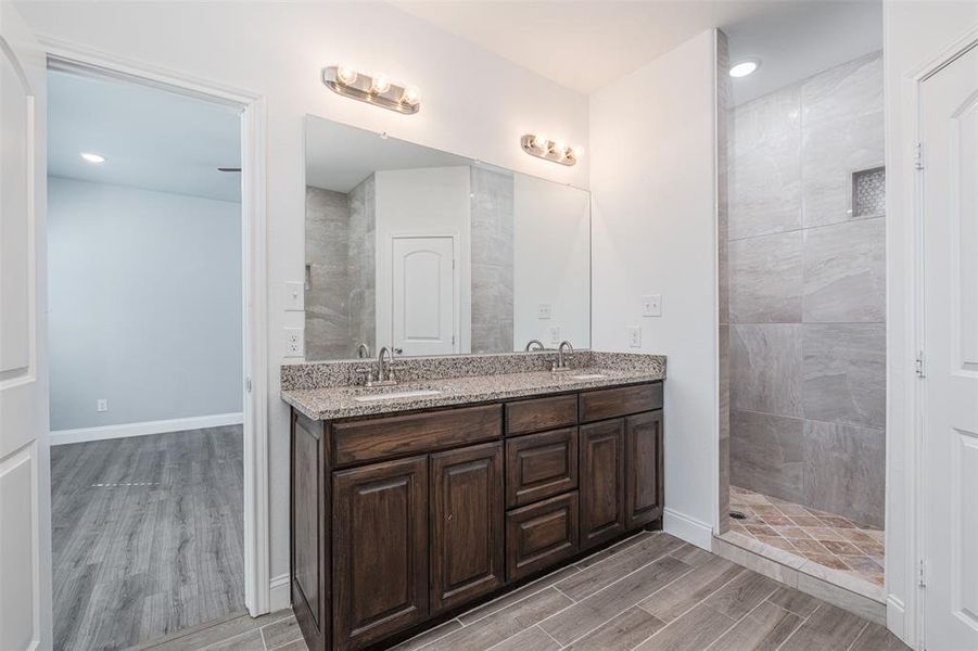 Full bath featuring double vanity, wood finish floors, a sink, and walk in shower