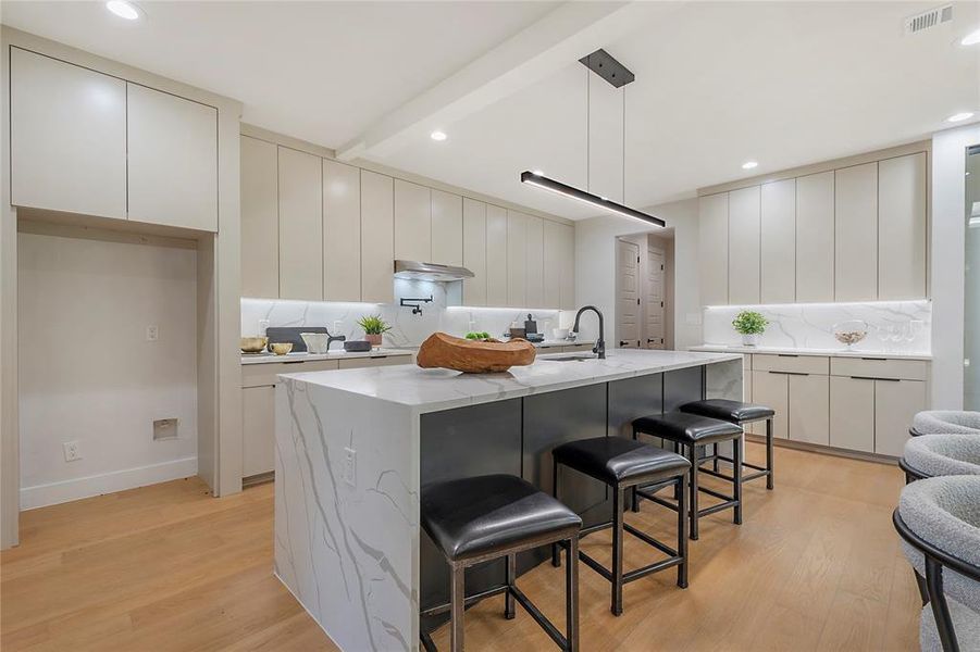 Kitchen with a kitchen bar, sink, hanging light fixtures, light hardwood / wood-style floors, and a kitchen island with sink