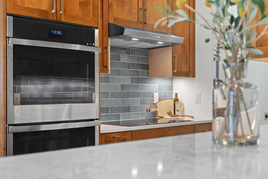 Kitchen with under cabinet range hood, black electric cooktop, backsplash, and light countertops Kitchen with under cabinet range hood, black electric cooktop, backsplash, and light countertops