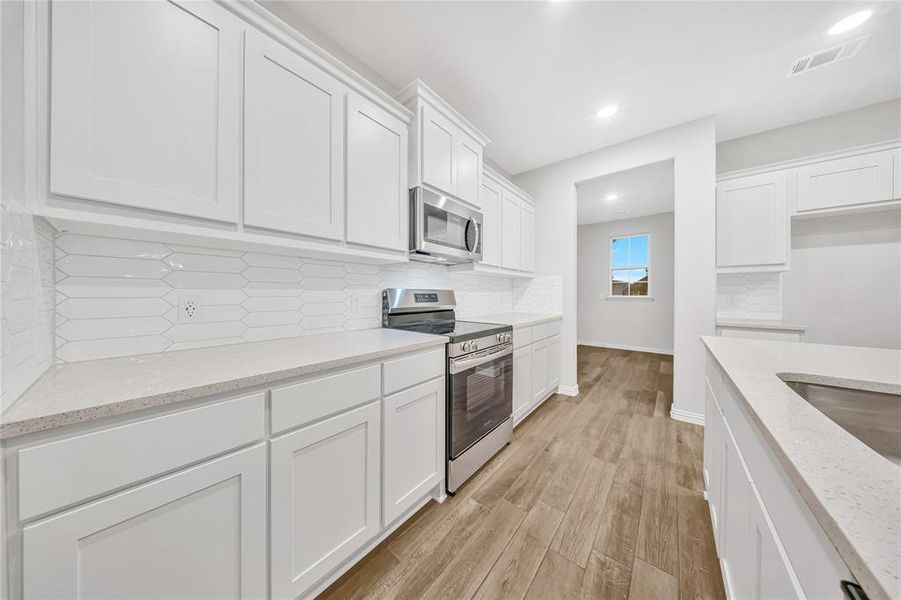 Kitchen with stainless steel appliances, white cabinetry, light wood-style flooring, tasteful backsplash, and light stone countertops Kitchen with stainless steel appliances, white cabinetry, light wood-style flooring, tasteful backsplash, and light stone countertops
