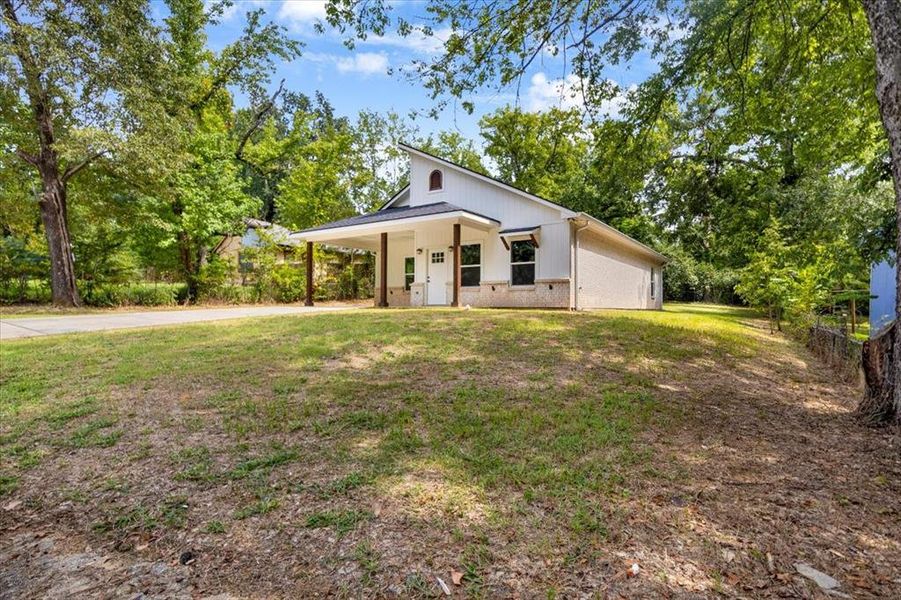 Modern farmhouse featuring brick siding, a porch, a front lawn, and an attached carport