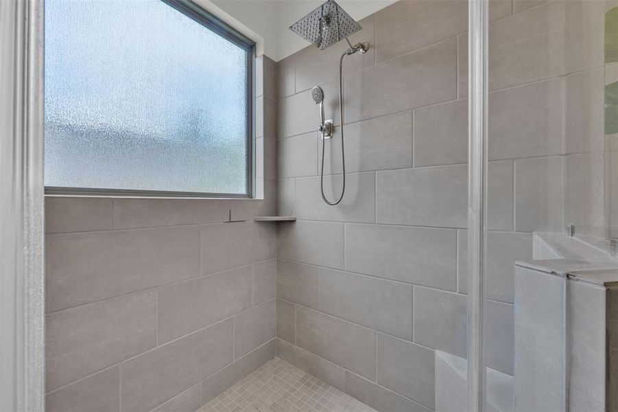 Contemporary shower enclosure featuring full-height light gray tilework, a frosted window, rain showerhead, handheld spray, and integrated shelving Contemporary shower enclosure featuring full-height light gray tilework, a frosted window, rain showerhead, handheld spray, and integrated shelving