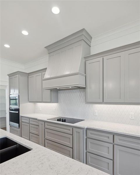 Kitchen featuring gray cabinetry, stainless steel appliances, light stone counters, and custom range hood