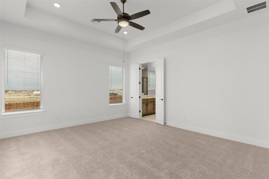Unfurnished bedroom featuring a raised ceiling, light carpet, multiple windows, and recessed lighting