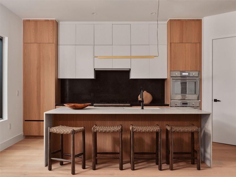 Kitchen with dual tone cabinetry, a breakfast bar area, modern cabinets, light wood-style flooring, and light stone counters