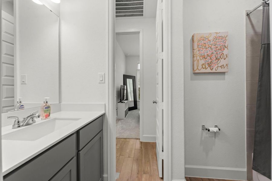 3rd full bathroom  for bedrooms 3 and 4 includes a single vanity with rectangular undermount sink and quartz countertop, wood-look tile flooring, toilet, and rectangular-tiled shower/tub combo with toiletry shelf and removable hand-held shower head.