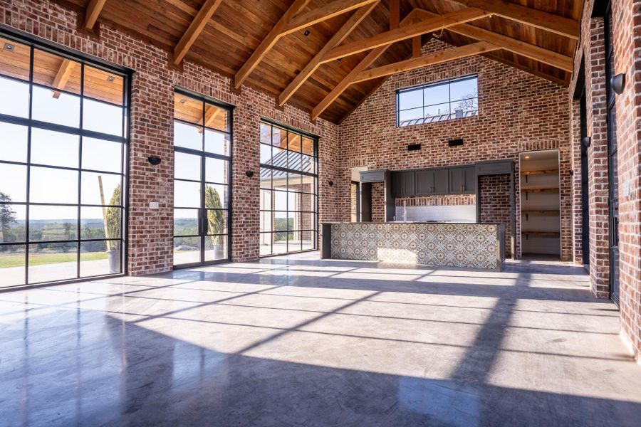 Unfurnished living room with high vaulted ceiling, brick wall, concrete floors, and a wood ceiling with exposed beams