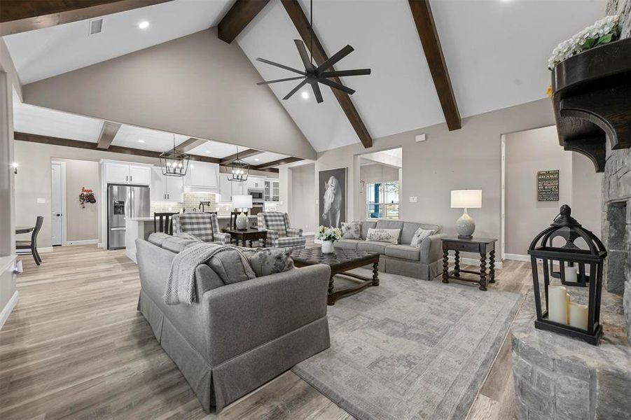 Living room with high vaulted ceiling, ceiling fan with notable chandelier, a stone fireplace, light hardwood / wood-style flooring, and beam ceiling