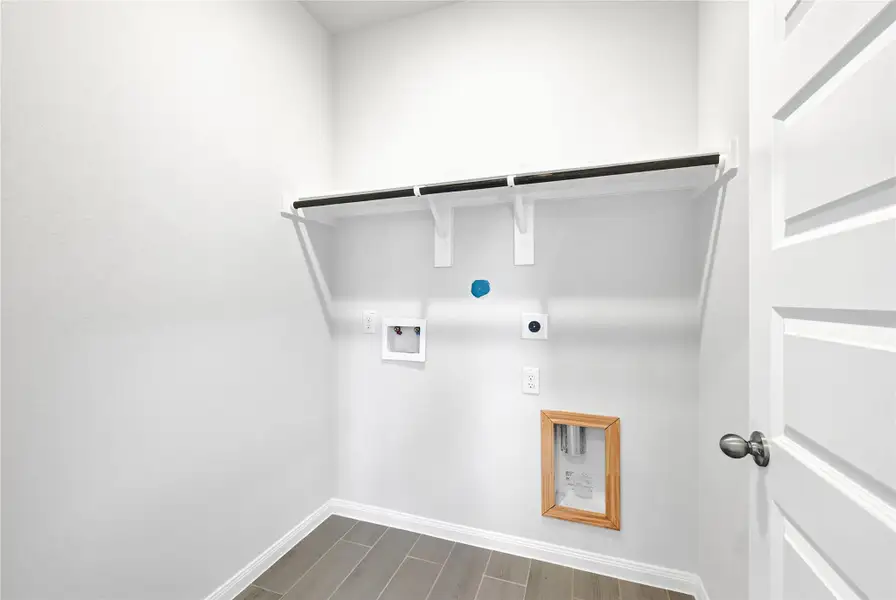 This photo shows a utility room with hookups for a washer and dryer, featuring wall-mounted shelving and tile flooring.Please note: The image is not the actual home; it is a home with the same floor plan in the neighborhood.
