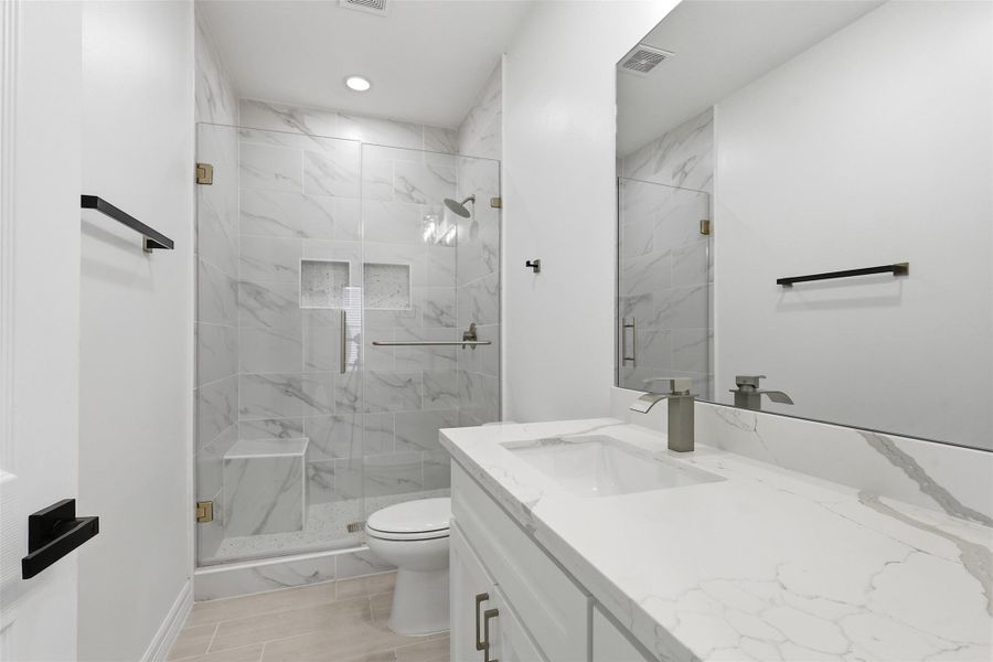 Upstairs bathroom walk in shower with black frame glass door and floor to ceiling marble look tile walls.