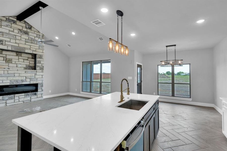 Kitchen featuring a stone fireplace, decorative light fixtures, light stone counters, a center island with sink, and open floor plan