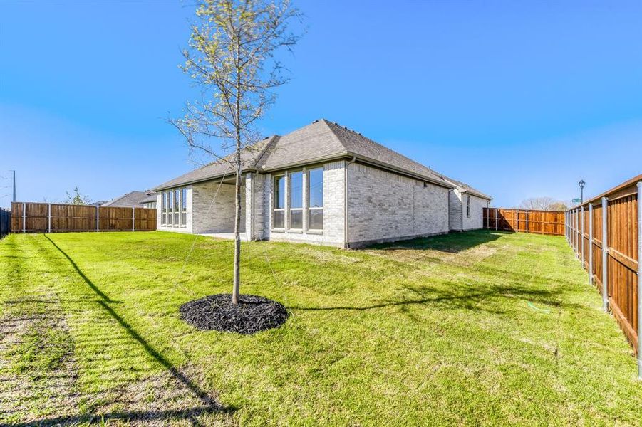 Rear view of property with brick siding, a fenced backyard, roof with shingles, and a patio area