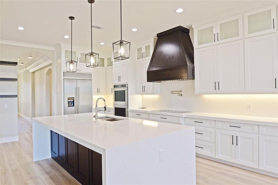 Kitchen featuring premium range hood, sink, an island with sink, white cabinetry, and stainless steel appliances