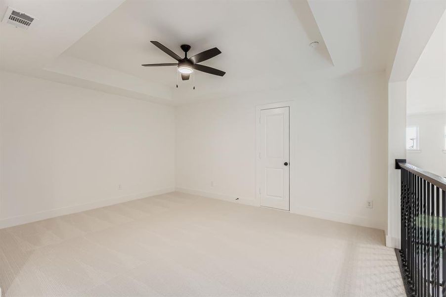 Unfurnished room featuring a tray ceiling, light carpet, and a ceiling fan
