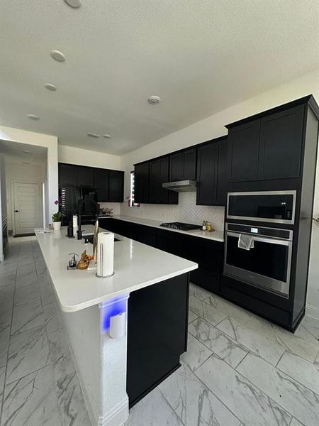 Kitchen with decorative backsplash, a center island with sink, a textured ceiling, and gas cooktop