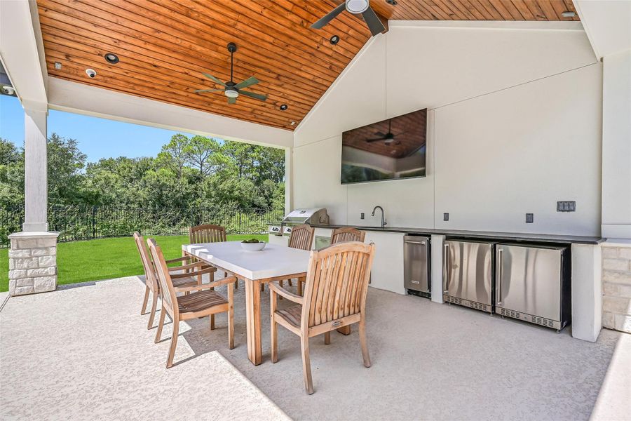 Built for serious outdoor entertaining, the kitchen includes a Napoleon gas grill, separate gas burner, sink, dual undercounter refrigerators, ice maker, extensive counter space and mounted TV beneath the vaulted wood-plank ceiling.