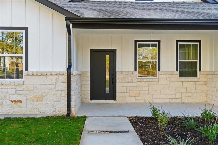 Doorway to property with board and batten siding, a shingled roof, stone siding, and a porch