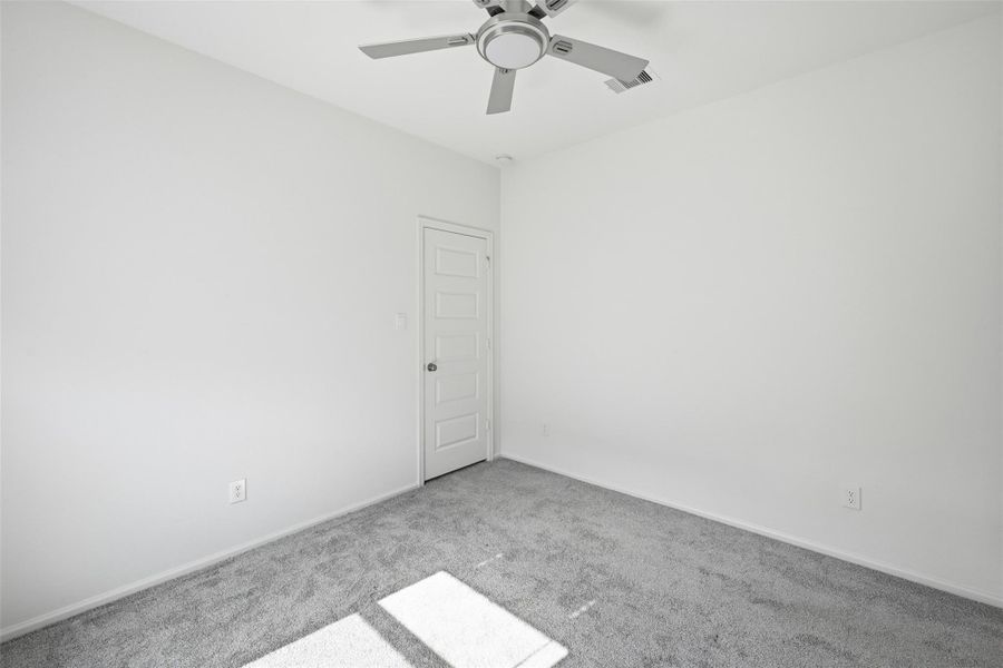 Bright and airy room featuring fresh white walls, plush gray carpeting, and a sleek ceiling fan for comfort.