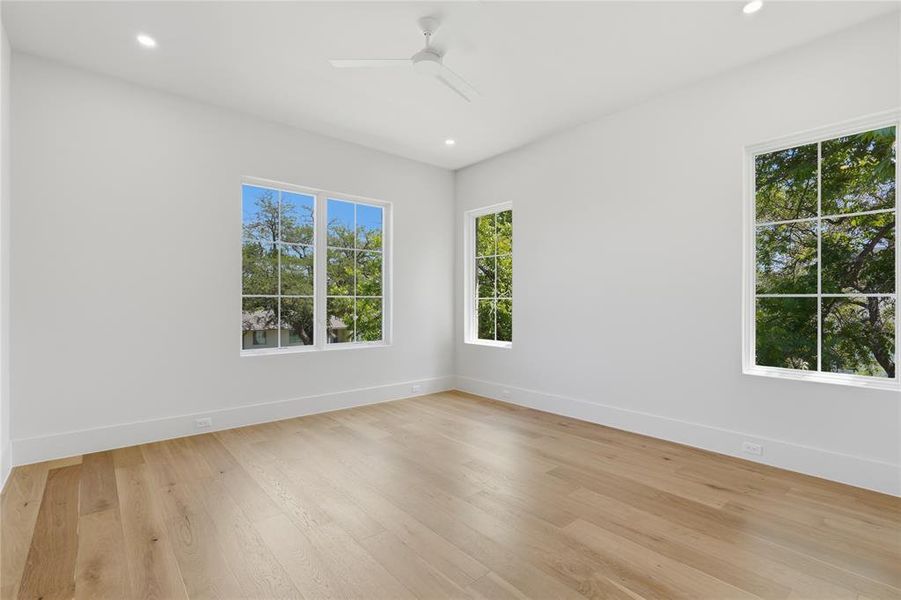 Secondary bedroom with tree canopy views, wide-plank hardwood floors, and ceiling fan Secondary bedroom with tree canopy views, wide-plank hardwood floors, and ceiling fan