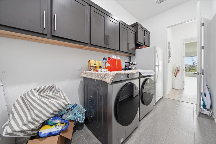 The laundry area features dark grey cabinetry with silver hardware, a washer and dryer, and grey tiled flooring