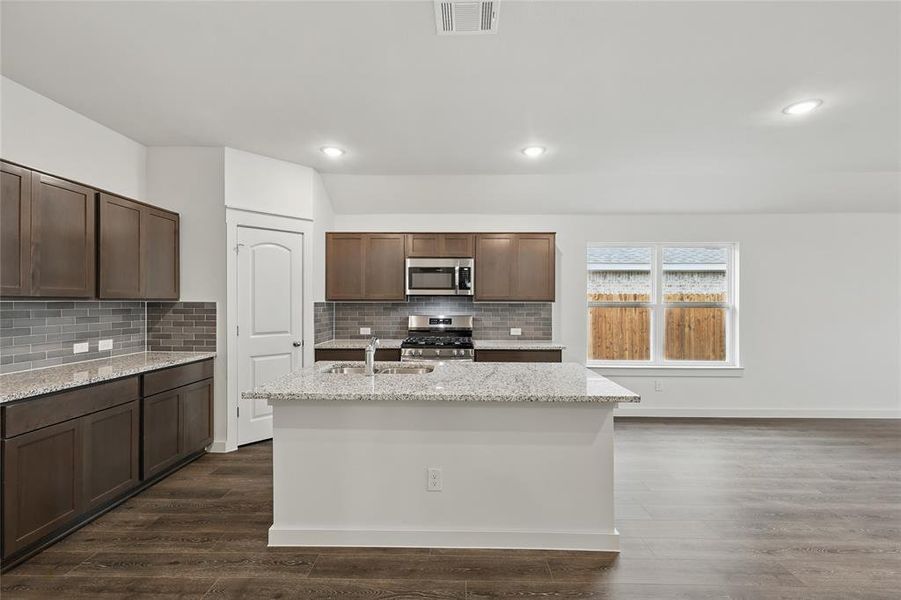 Kitchen featuring stainless steel appliances, light stone countertops, dark wood finished floors, a center island with sink, and dark wood finish cabinetry Kitchen featuring stainless steel appliances, light stone countertops, dark wood finished floors, a center island with sink, and dark wood finish cabinetry