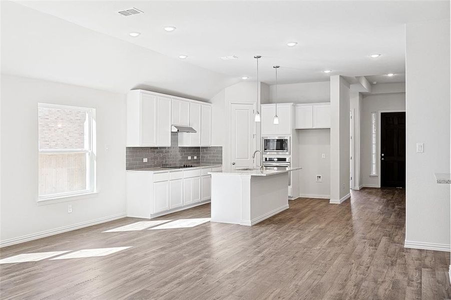 Kitchen featuring appliances with stainless steel finishes, light hardwood / wood-style flooring, pendant lighting, and an island with sink