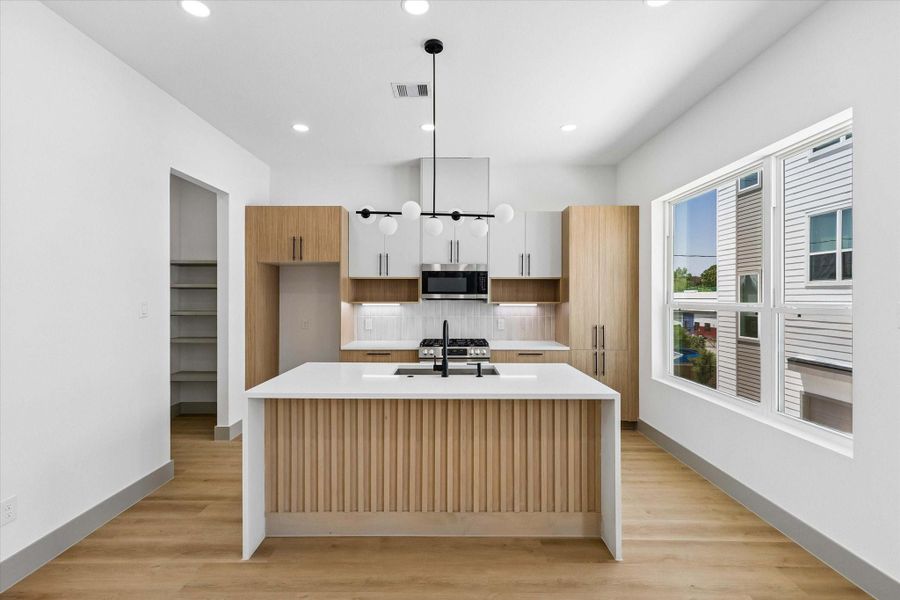 European inspired design shines through warm wood cabinetry, quartz countertops, matte black fixtures, and a waterfall island with fluted detailing that anchors the room with warmth and texture. European inspired design shines through warm wood cabinetry, quartz countertops, matte black fixtures, and a waterfall island with fluted detailing that anchors the room with warmth and texture.