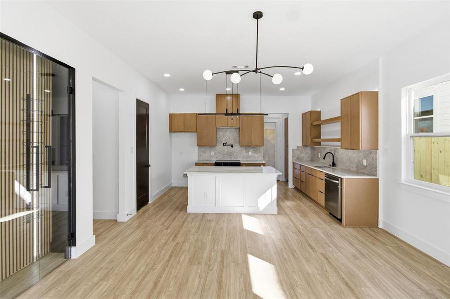 Kitchen with hanging light fixtures, a center island, light wood-style floors, wood finish cabinetry, and tasteful backsplash