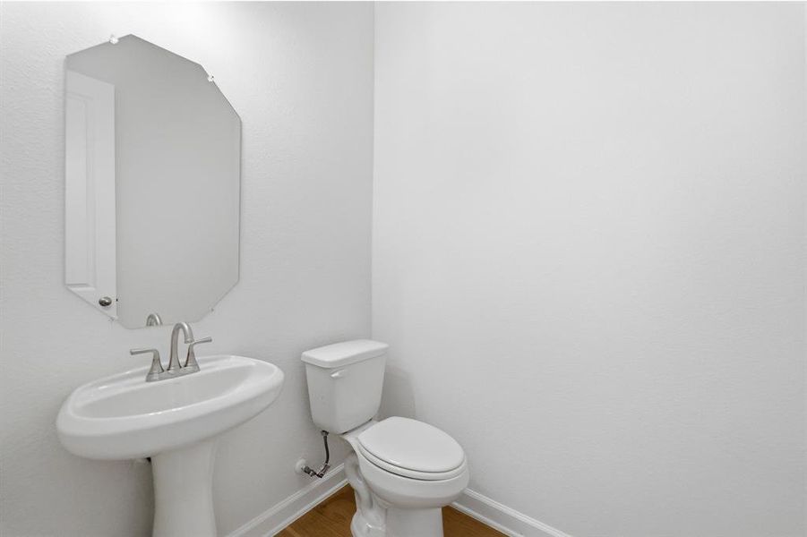 Pedestal sink with chrome faucet, octagonal wall mirror, and wood-finish flooring
