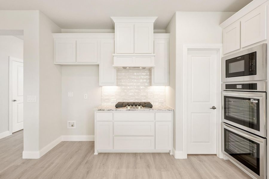 White kitchen with gas cooktop, custom range hood, double wall oven, and light wood floors