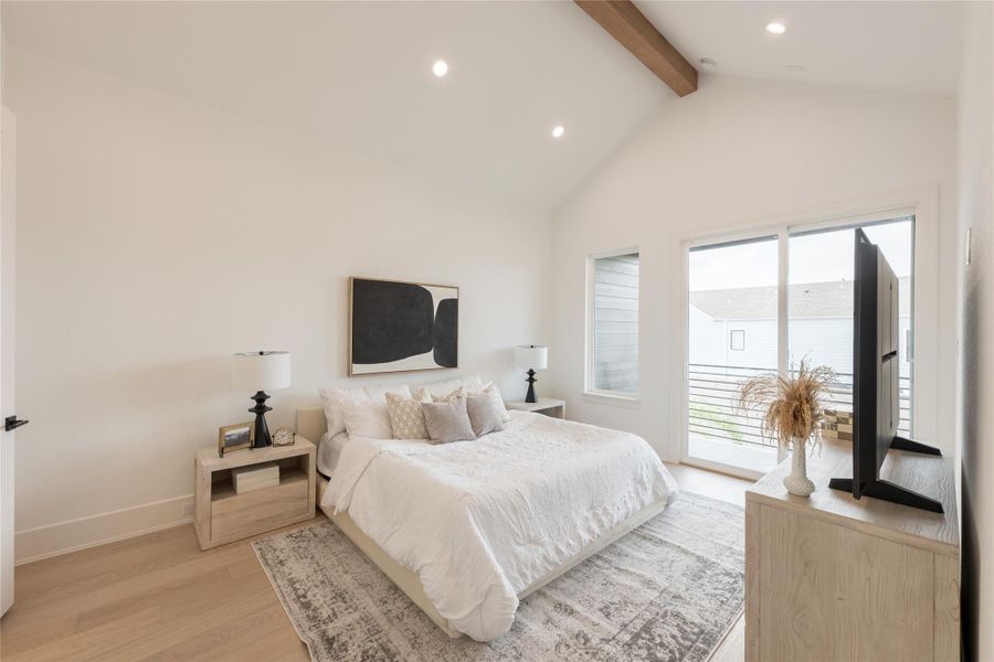 A primary bedroom that reaches for the ceiling. A natural-wood ridge beam runs the length of the pitched volume, holding cathedral geometry overhead while sliders open the exterior wall to a private balcony. Room enough to breathe.