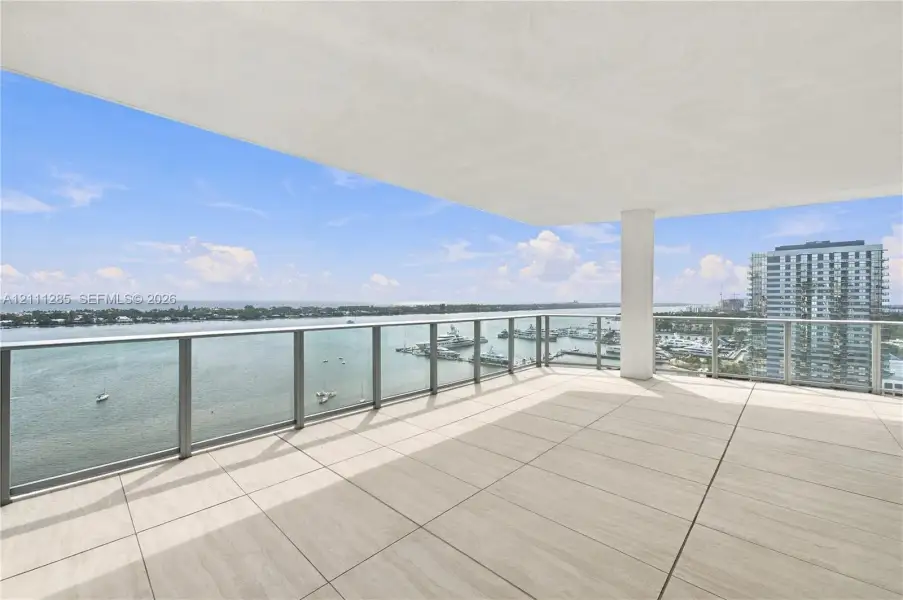 Expansive covered balcony featuring large-format stone-finish tile flooring and a glass-paneled railing with brushed metal trim Expansive covered balcony featuring large-format stone-finish tile flooring and a glass-paneled railing with brushed metal trim