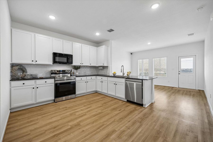 Kitchen with stainless steel appliances, white cabinets, a peninsula, decorative backsplash, and recessed lighting