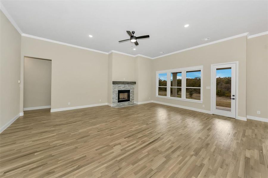 Unfurnished living room featuring ceiling fan, a stone fireplace, ornamental molding, and light hardwood / wood-style flooring