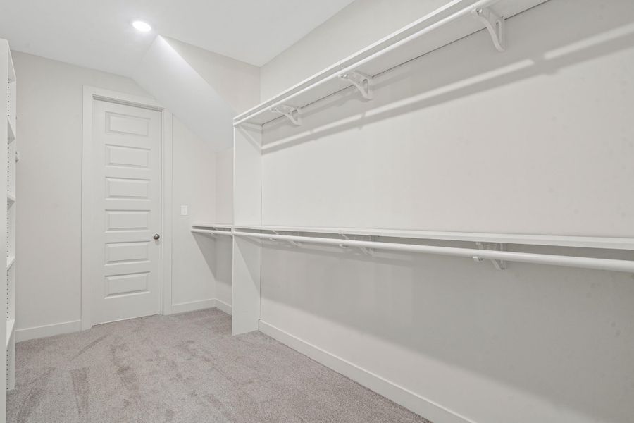 Spacious storage area featuring light gray carpeting, white walls, recessed lighting, and built-in white shelving and hanging rods Spacious storage area featuring light gray carpeting, white walls, recessed lighting, and built-in white shelving and hanging rods