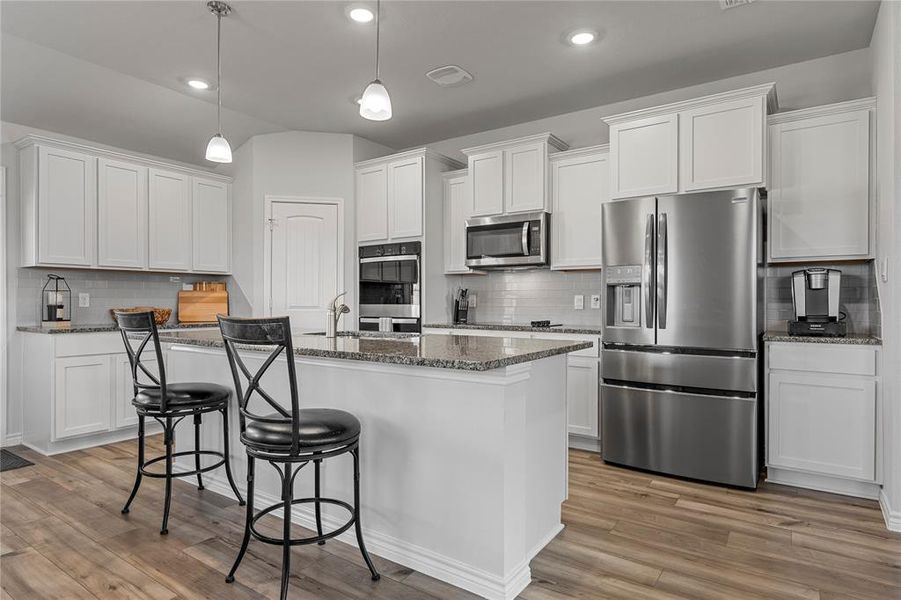 Kitchen with stainless steel appliances, white cabinets, a breakfast bar, dark stone counters, and recessed lighting