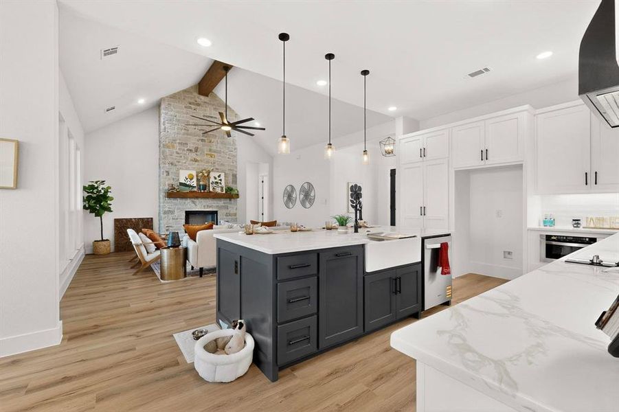 Kitchen featuring dual tone cabinets, light wood-style flooring, light stone countertops, a center island with sink, and open floor plan