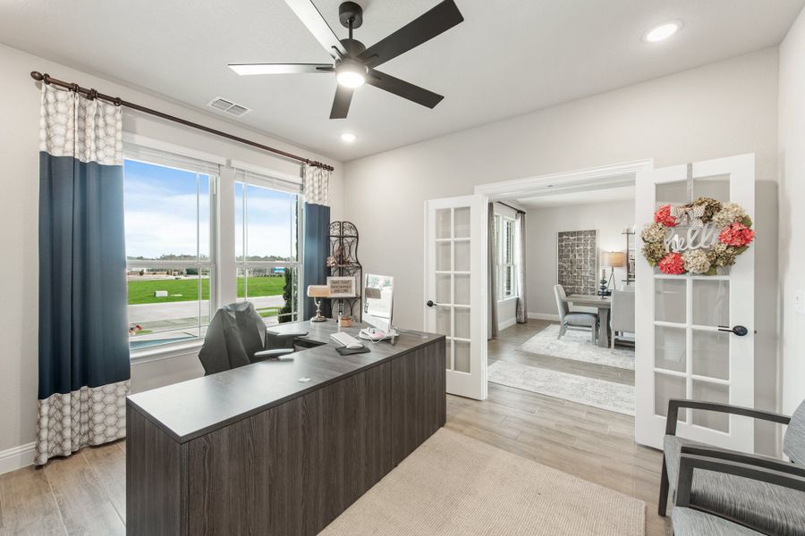 Home office with dark wood desk, ceiling fan, French doors, and large window with backyard view Home office with dark wood desk, ceiling fan, French doors, and large window with backyard view