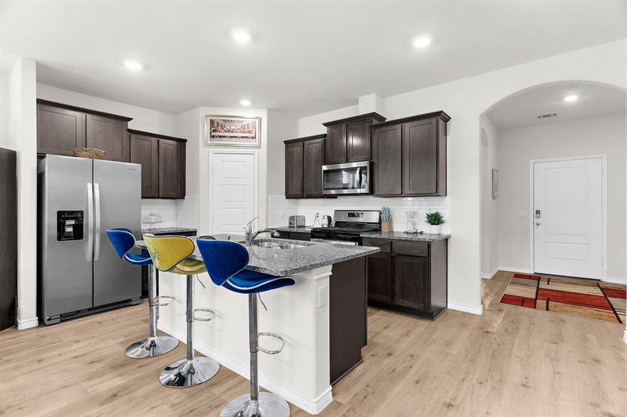 Kitchen with dark brown cabinetry, a sink, light stone countertops, stainless steel appliances, and arched walkways